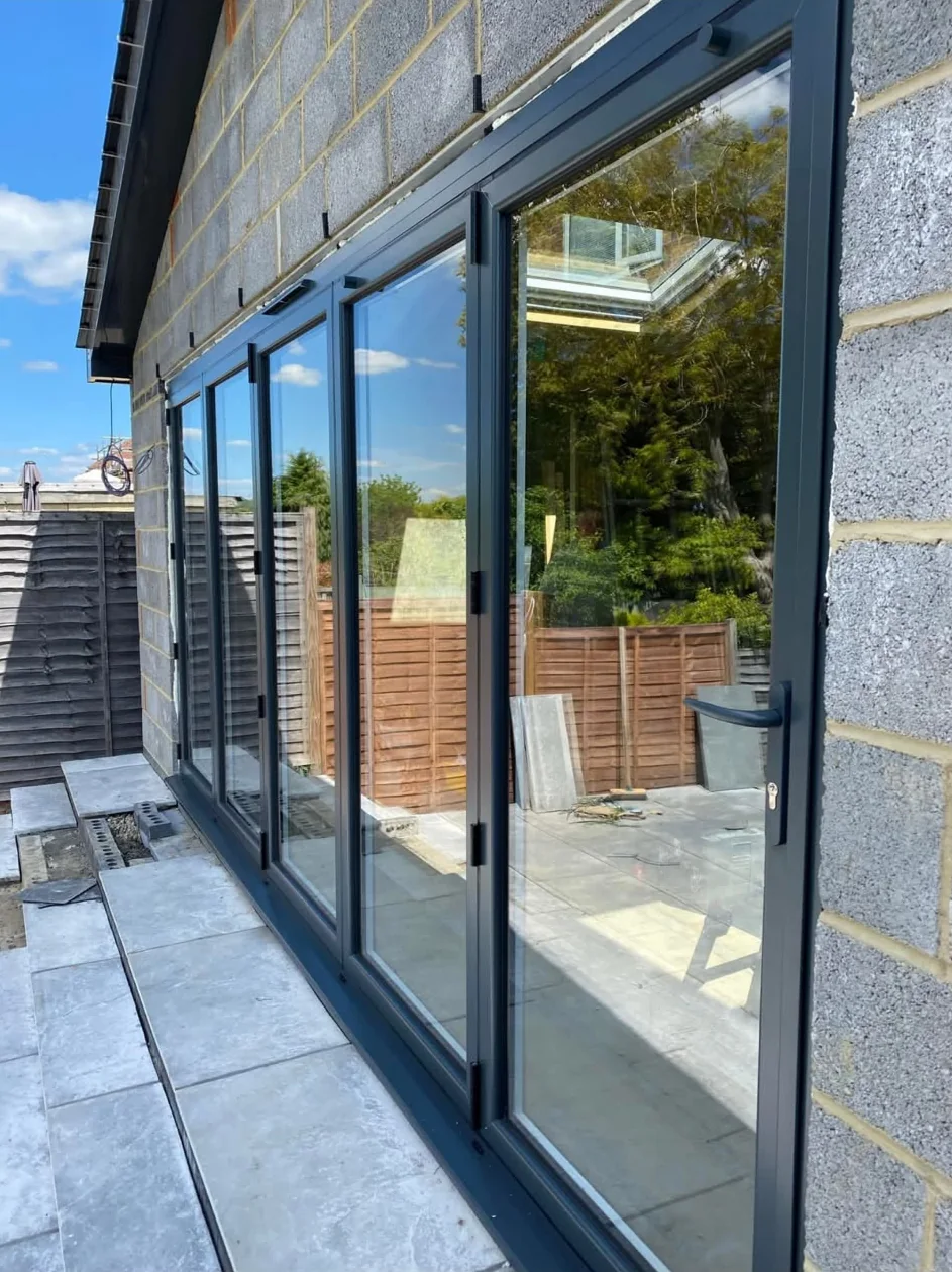 A dark grey five-pane bifold door set into a blockwork extension, facing a paved garden