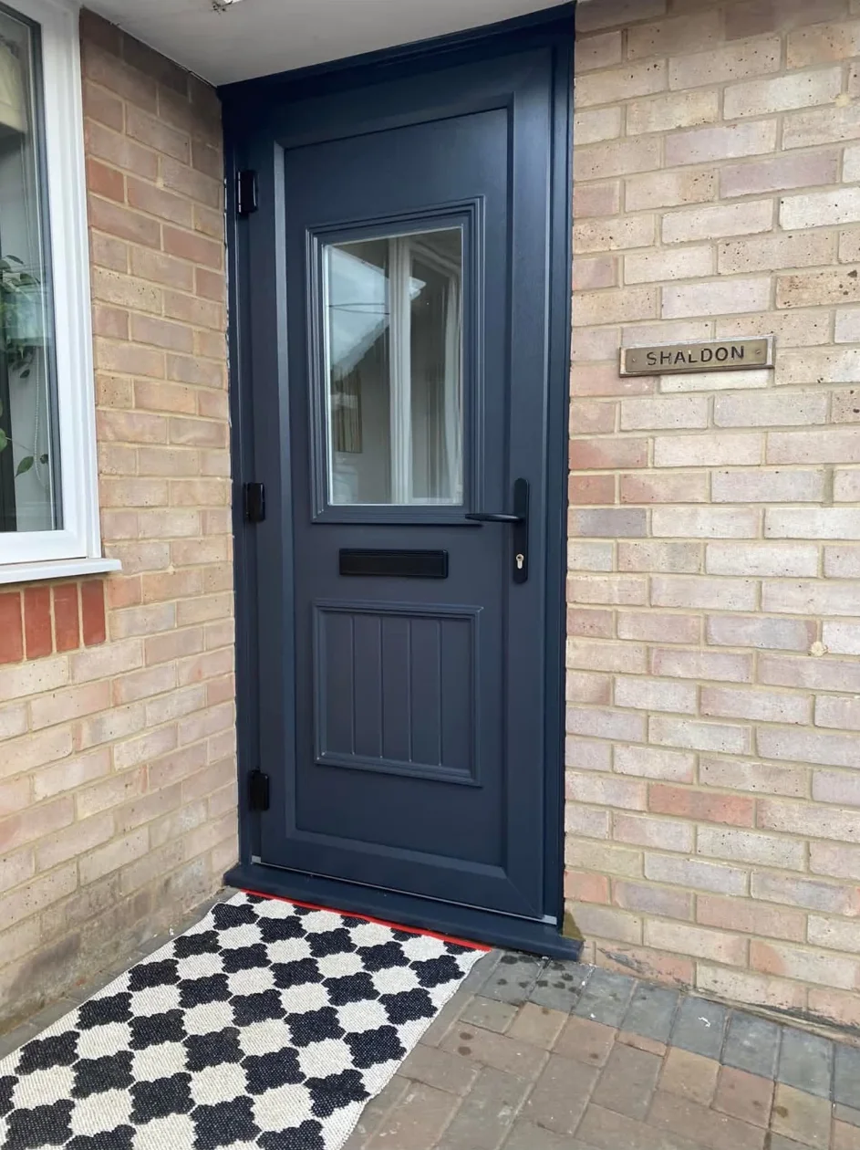 A dark grey front door with a glazed upper panel and black hardware, set into pale brick
