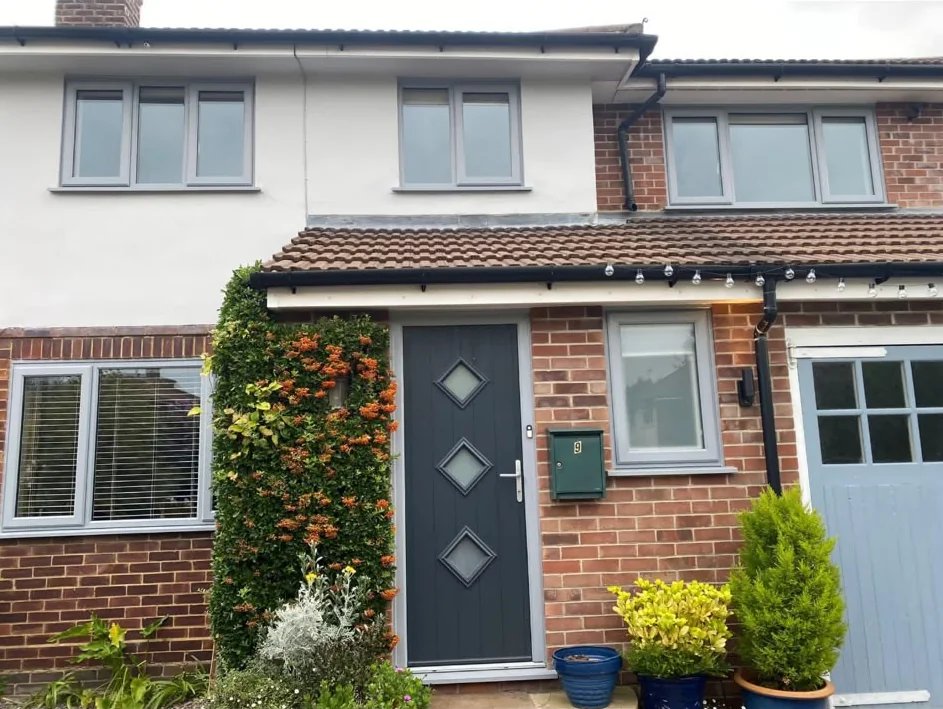 A house front with light grey window frames and a dark grey door with three diamond glass panels
