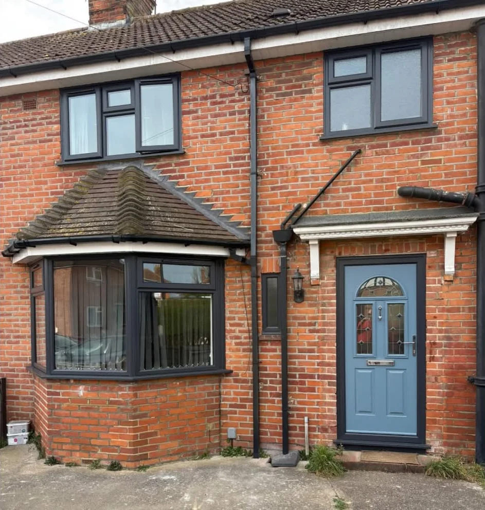 A red-brick terraced house with new dark grey windows, a dark grey bay window and a pale blue front door